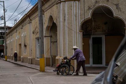 Un hombre empuja una silla de ruedas frente a un hotel quemado por el narcotráfico en la plaza principal de Aguililla.