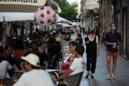 Dos personas pasean por una calle llena de terrazas en el barrio barcelonés del Poblesec