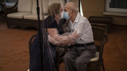 Una mujer abraza y besa a su marido a través de una pantalla de plástico para evitar contraer el coronavirus en una residencia de ancianos en Barcelona.