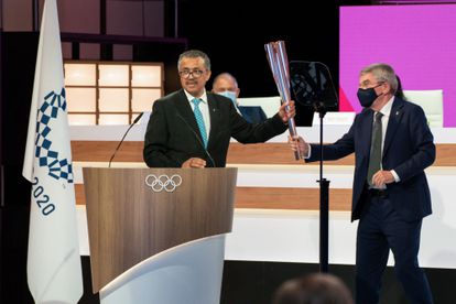 El director general de la OMS, a la izquierda, recibe del presidente del COI la antorcha olímpica.