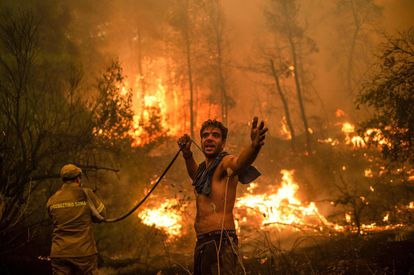 Un residente de la localidad de Pefki, en la isla de Eubea, hace un gesto mientras sostiene una manguera de agua vacía durante un intento de extinguir los incendios forestales que golpean a Grecia desde hace días.