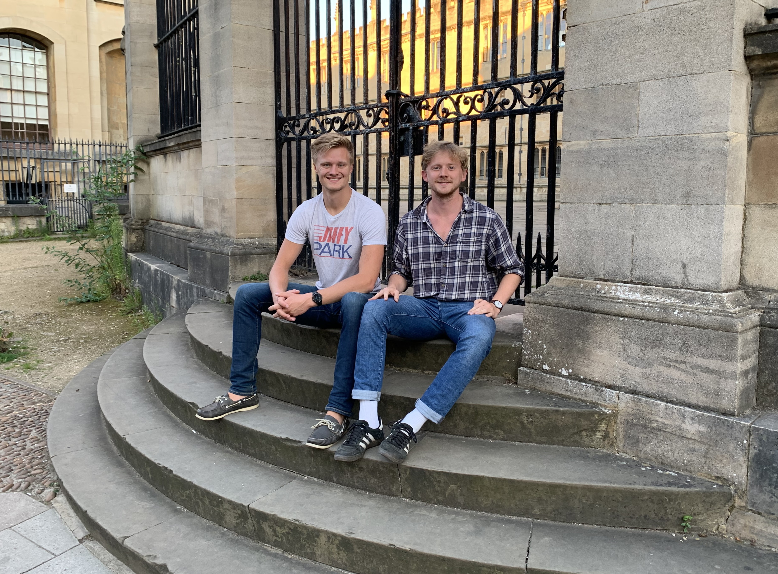 Los fundadores de Heimdal, Marcus Lima (izquierda) y Erik Millar, sentados junto a una puerta de metal sobre escalones de piedra.
