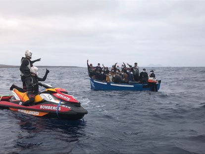 Dos bomberos indican a 24 inmigrantes de una patera localizada frente a la costa de Pedro Barba, en La Graciosa (Canarias), que esperen a un barco de Salvamento Marítimo.