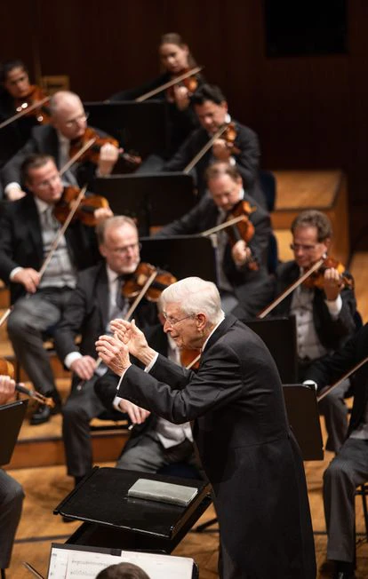 Herbert Blomstedt, con un gesto muy característico, dirige la Cuarta Sinfonía de Anton Bruckner. Obsérvese la partitura de bolsillo, sin abrir, sobre el atril del director.