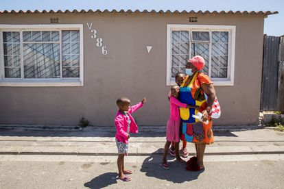 Elda Sidlabane (66) es recibida por Yamihla Lambatha (6) y Achumile Lambatha (10), sus nuevos nietos adoptivos, cuando llega a casa de su reunión de grupo de personas mayores en su vecindario del municipio de Khayalitsha, fuera de Ciudad del Cabo, Sudáfrica, el 19 de febrero de 2021.