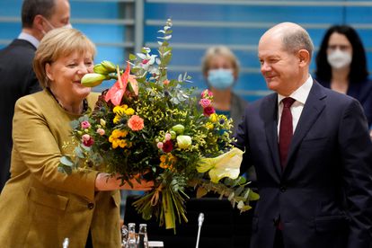 La canciller alemana en funciones, Angela Merkel, recibe un ramo de flores de su previsible sucesor, Olaf Scholz, esta mañana antes del que probablemente sea su último consejo de ministros.