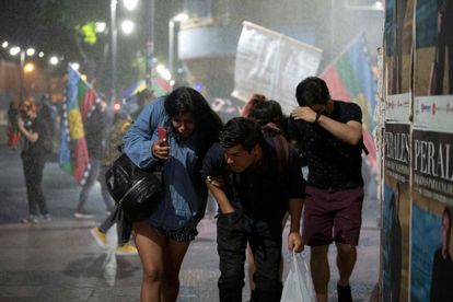 La gente huye de un cañón de agua utilizado por la policía antidisturbios durante una manifestación contra el candidato presidencial chileno José Antonio Kast y sus propuestas en la Plaza Italia de Santiago, el 17 de diciembre de 2021, antes de la segunda vuelta de las elecciones presidenciales del domingo.