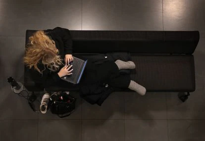 Una joven utiliza su ordenador tumbada en un sofá de la biblioteca.