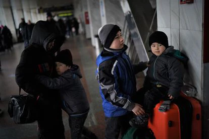 Islam, 12, en el centro, cuida de su hermano Yasín, 4, mientras otro hermano, Illias, de siete, se abraza a su madre, en la estación de Kiev.