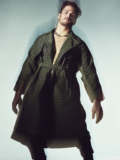 El modelo y jugador de fútbol americano Jon Toth viste abrigo de algodón negro y verde con anagrama All Over de Loewe. Collares de Bershka.