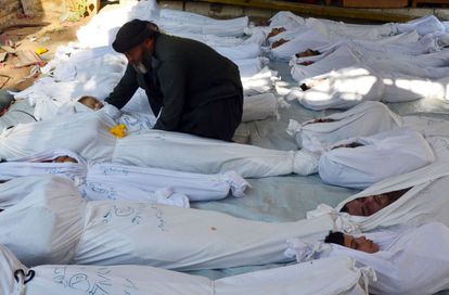 Un hombre sostenía el cuerpo de un niño muerto entre los cadáveres envueltos en sudarios, en 2013 en Guta, en la periferia de Damasco.