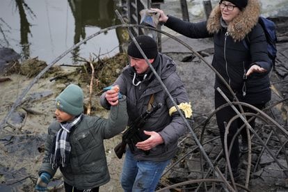 Un miliciano ayuda a varias personas a cruzar sobre los restos del puente sobre el río Irpin, a las afueras de Kiev.