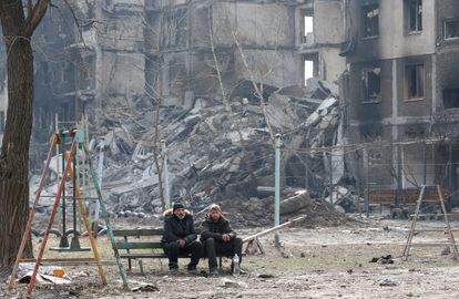 Dos vecinos sentados en un banco delante de edificios destruidos por los bombardeos en Mariupol, el 25 de marzo.