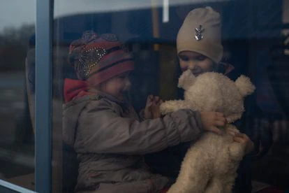 Dos niñas juegan con un oso de peluche mientras esperan la salida del autobús con destino al refugio temporal en Zaporiyia donde se alojan los refugiados que escapan de Mariupol y del Donbás. 