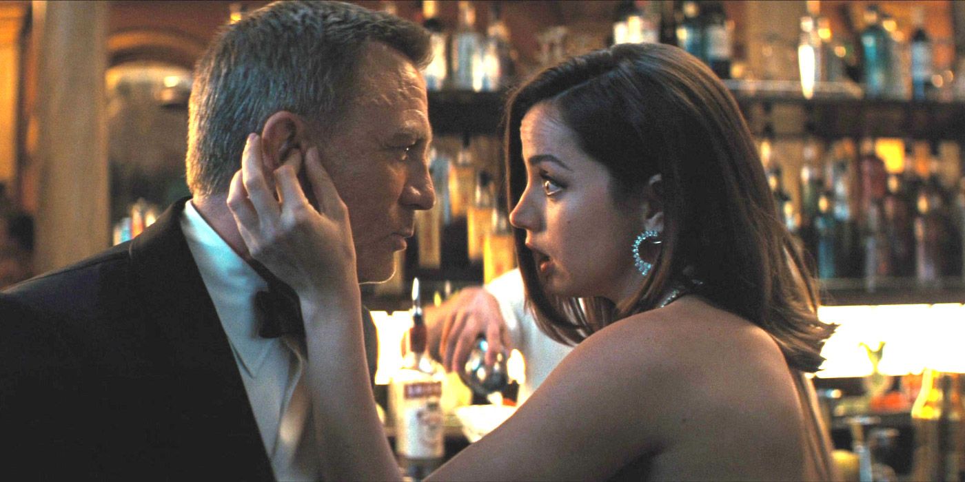 Daniel Craig as James Bond and Ana de Armas as Paloma in No Time to Die sharing a funny moment in a nightclub where they're sitting at the bar and she's playing with his ear