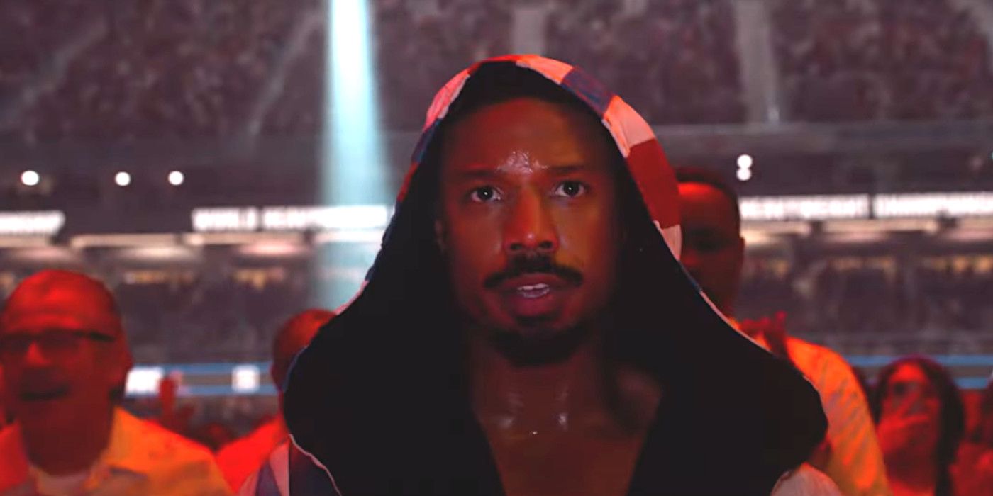Michael B. Jordan in Creed 3 walking into the boxing ring in a robe flooded with red light surrounded by a cheering crowd
