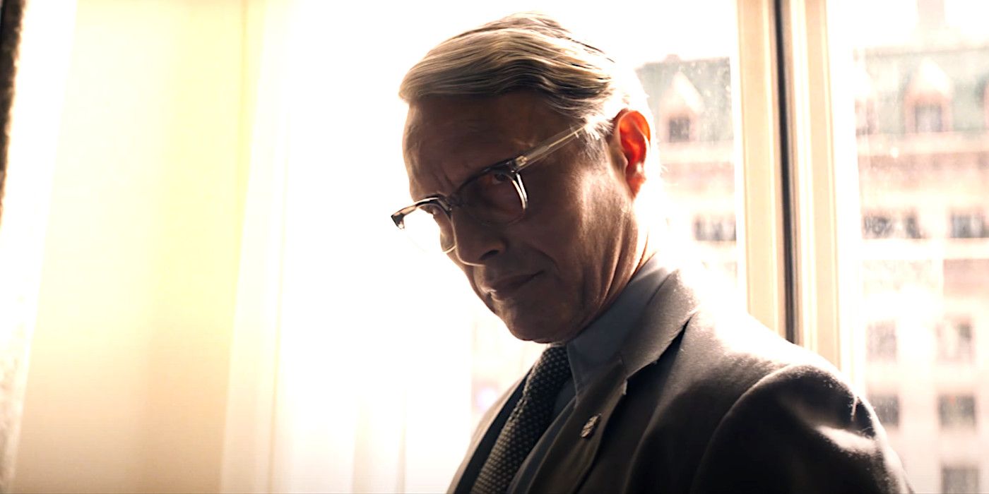 Mads Mikkelsen as Jurgen Voller in Indiana Jones 5 wearing glasses and a suit, looking menacing against a curtained window