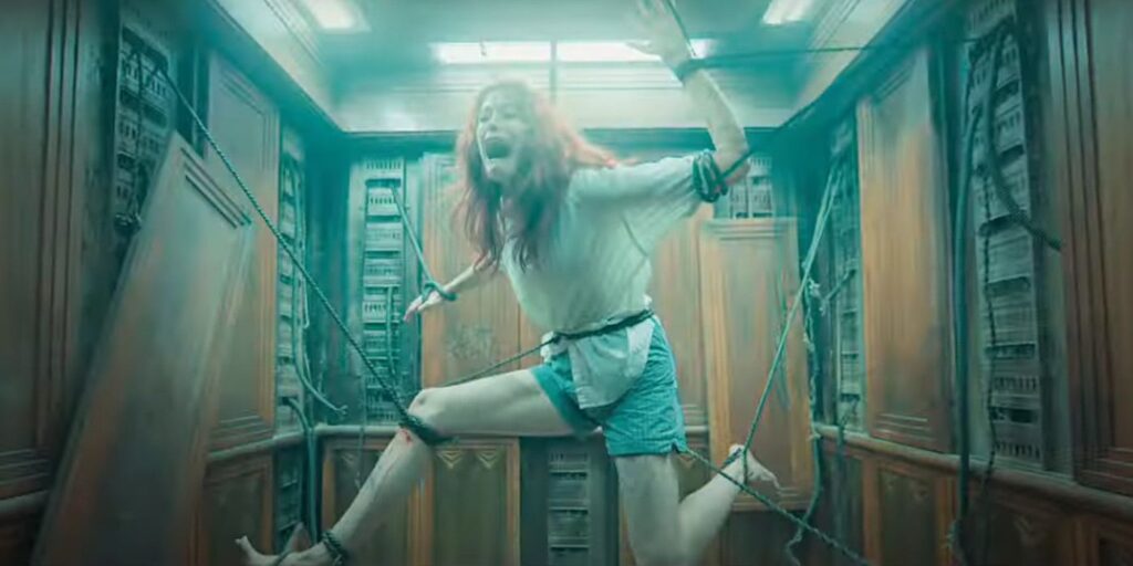 Alyssa Sutherland as Ellie in Evil Dead Rise in an elevator screaming with terror as ropes hold her in an unnatural position