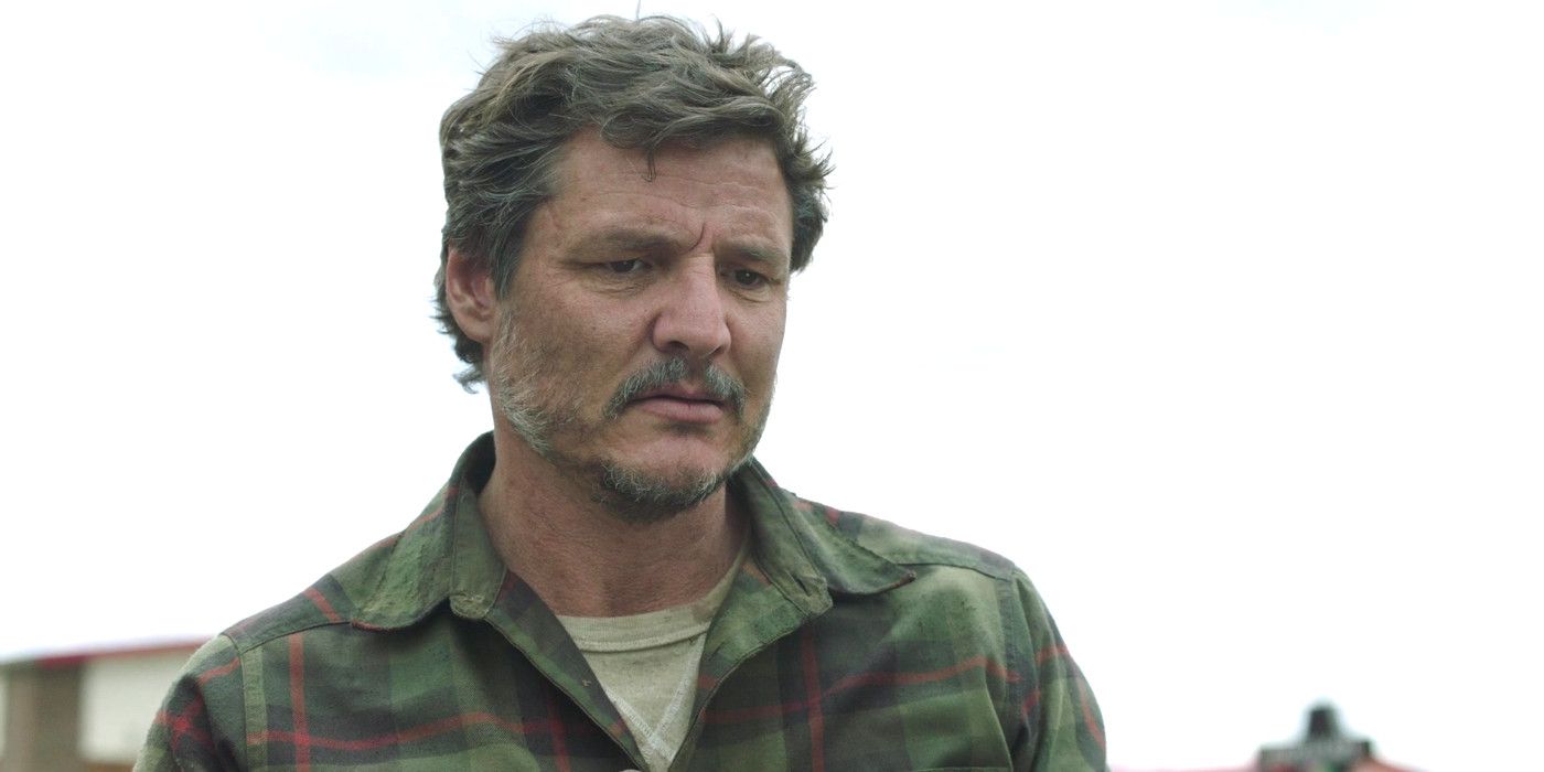 Pedro Pascal as Joel in The Last of Us gazing down with a somber expression on his face, a gray sky in the background