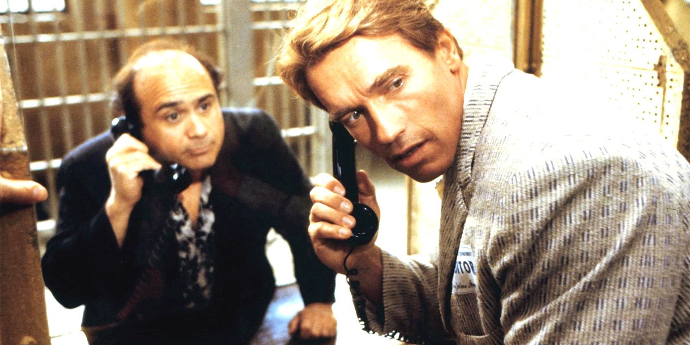 Danny DeVito and Arnold Schwarzenegger in Twins, holding phones in their hands on opposite sides of a jail window