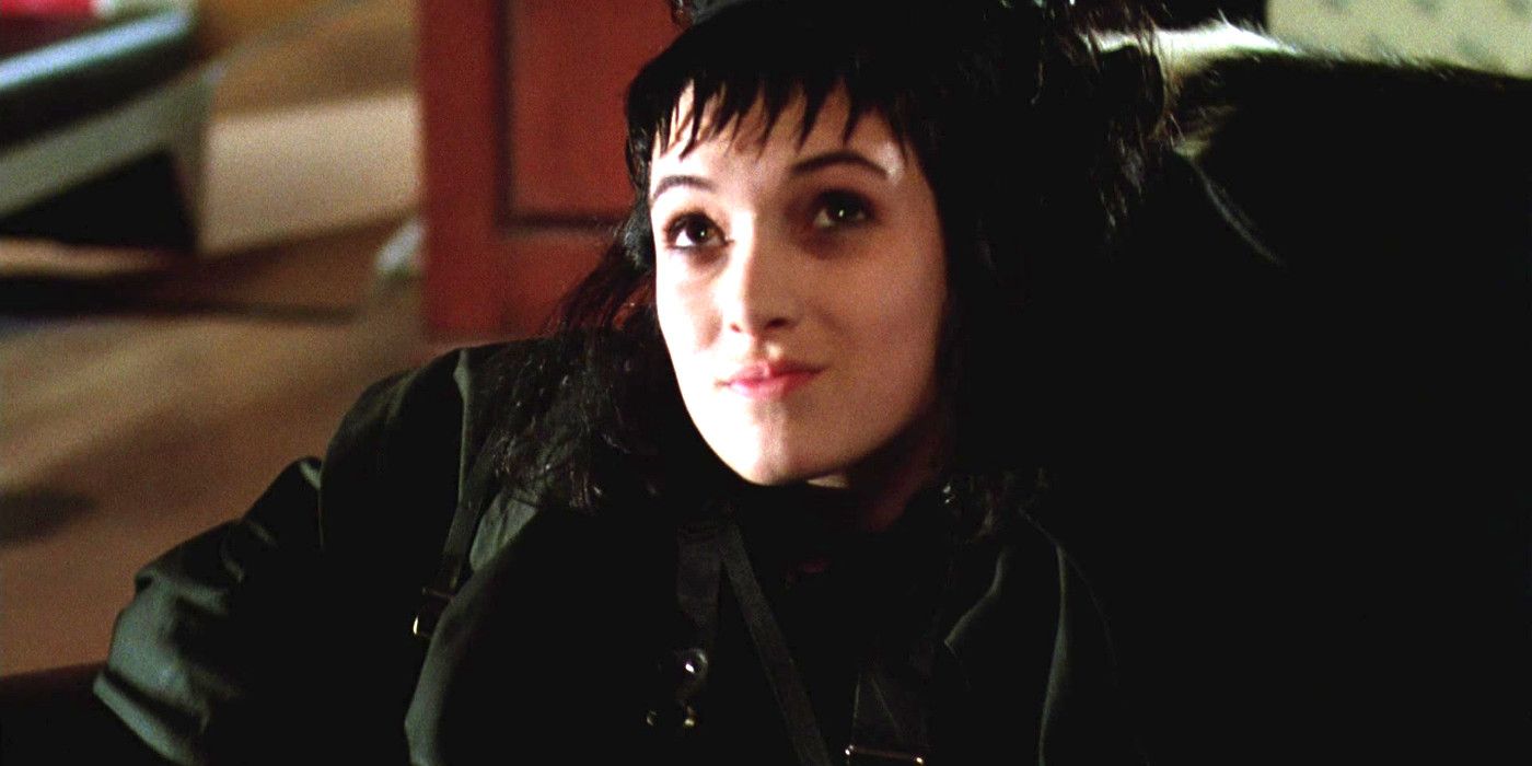 Winona Ryder as Lydia Deetz in Beetlejuice sitting in a chair all dressed in black with a pale face and jagged bangs, looking up sort of smugly