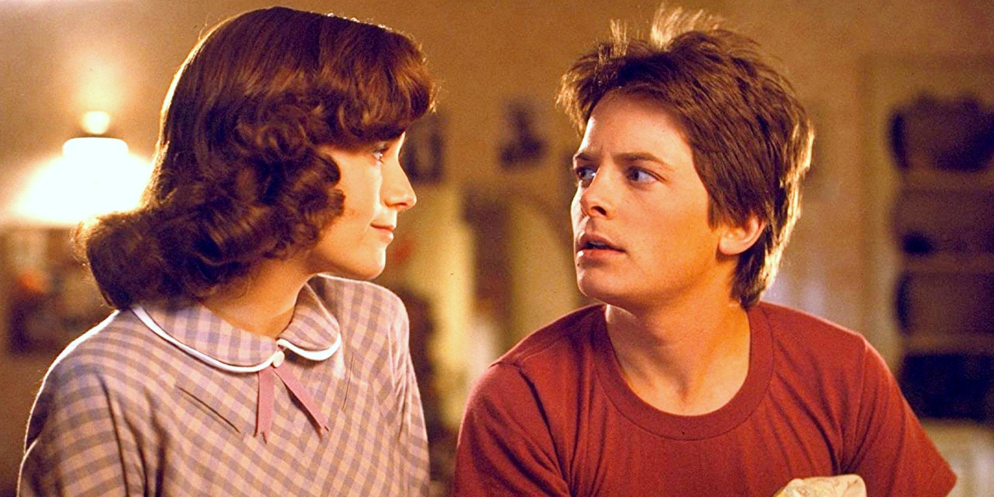 Lea Thompson and Michael J Fox in Back to the Future sitting on a bed and looking at each other