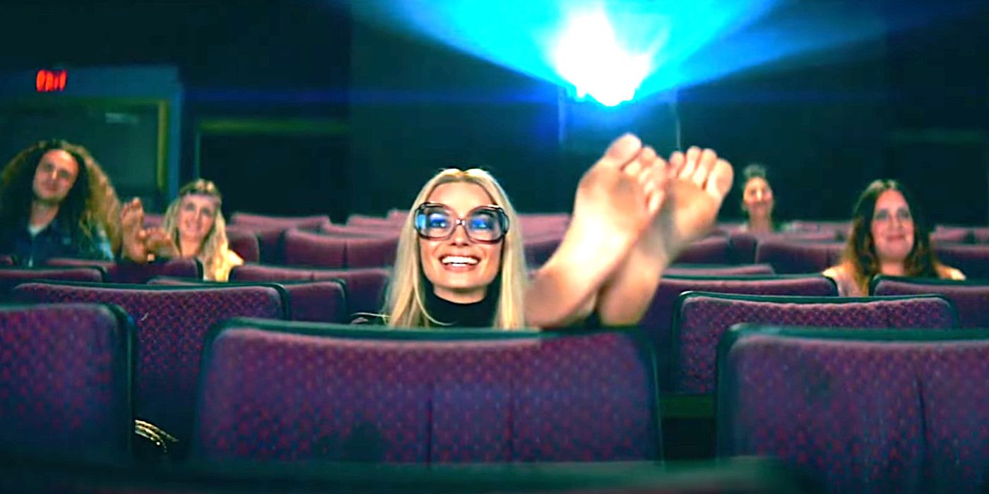 Margot Robbie As Sharon Tate In Once Upon A Time In Hollywood smiling while watching a movie, her dirty feet up on the theater seat in front of her