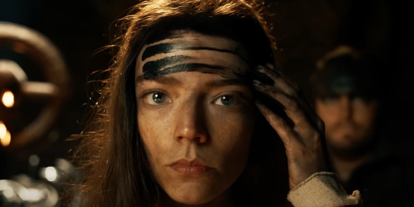 Furiosa (Anya Taylor-Joy) applies her war paint to her forehead while another soldier stoically stands by in the background in Furiosa