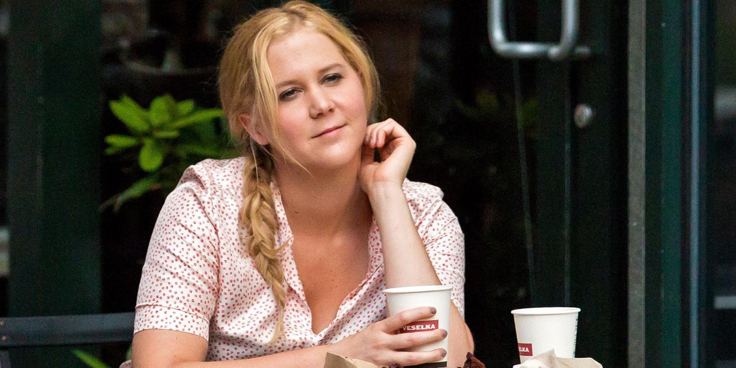 Amy Schumer sentada afuera con una expresión de ensueño en la cara en Trainwew